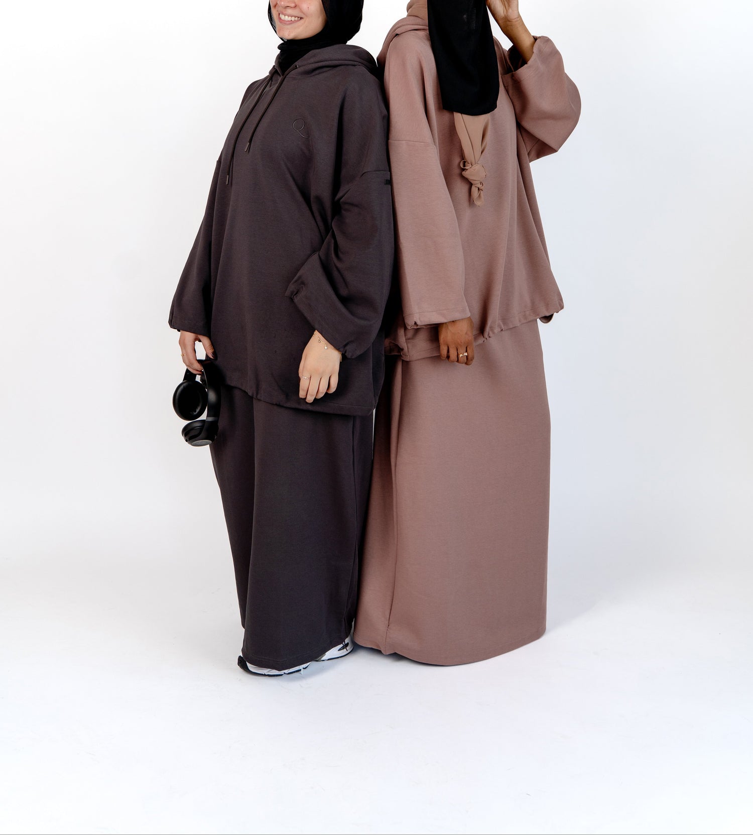 Two women wearing matching abayas in brown and black on a white background